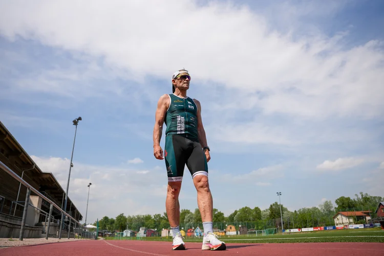 „Triathlet Paul Marouschek im grünen Wettkampfanzug steht auf einer Laufbahn und blickt in die Ferne“
